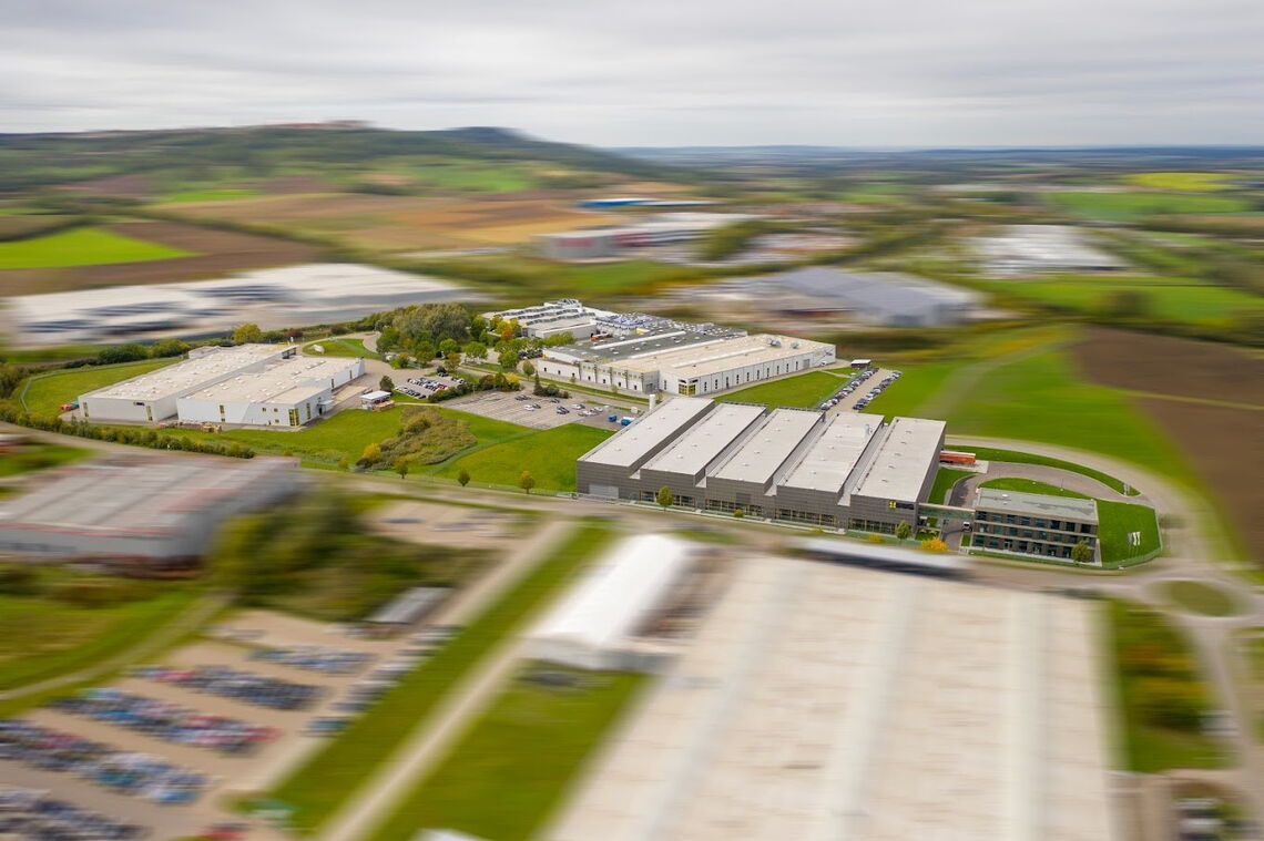 Luftaufnahme eines großen Industrieparks mit mehreren Gebäuden und grünen Flächen in einer ländlichen Gegend.