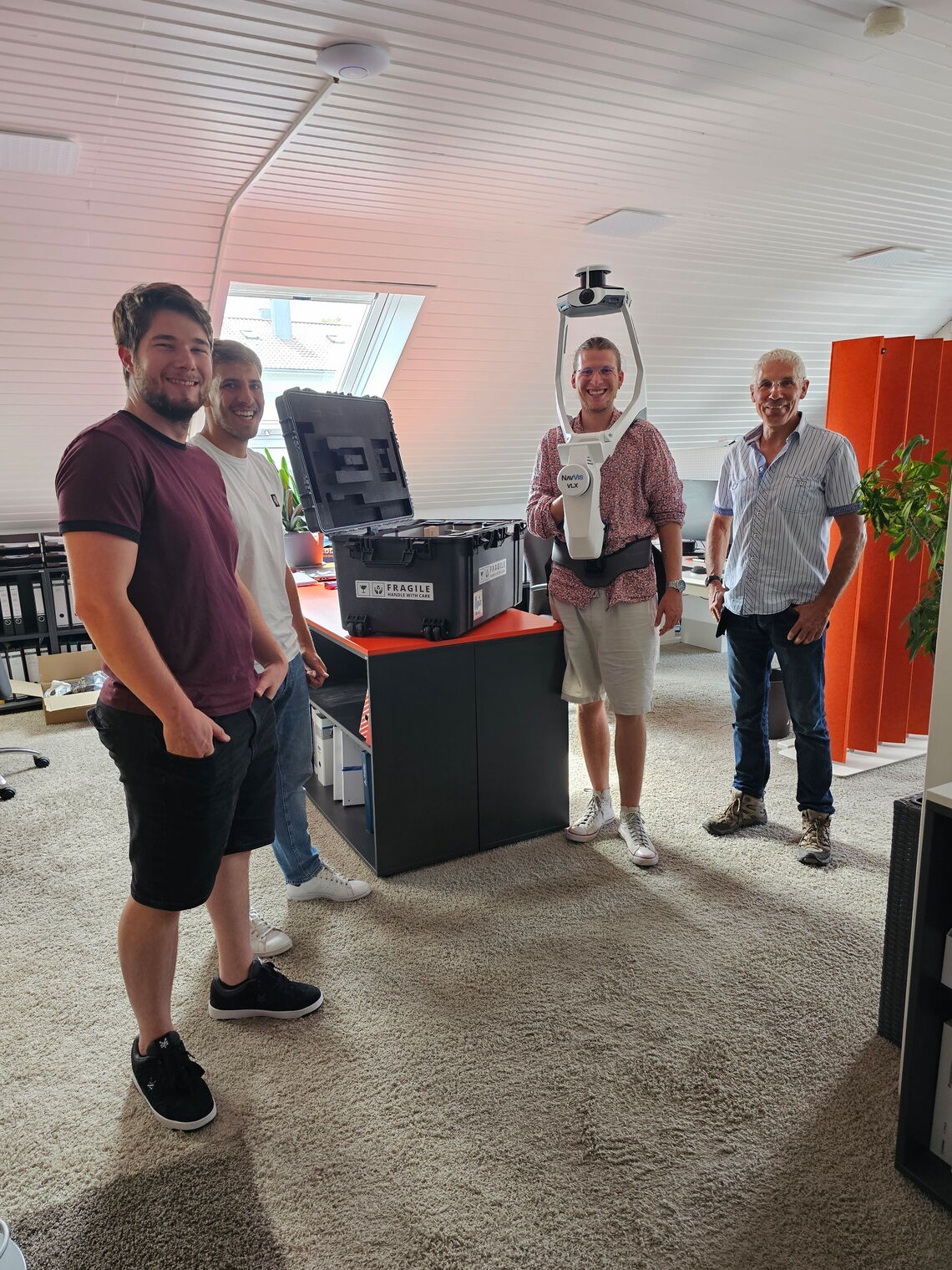 Eine Gruppe von Personen steht um einen modernen 3D-Scanner in einem Büro mit Teppichboden.